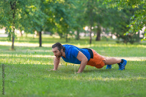 Middle aged man doing push-ups on the grass in park.