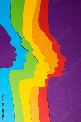 The gender-neutral rainbow-colored profiles are cut out of paper. The vertical paper art photo was made on a purple background. There is a place for text.