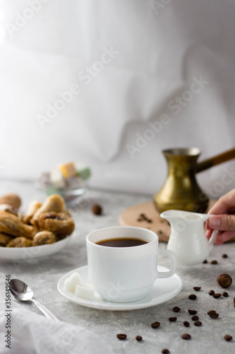 a woman s hand takes a milk jug and pours milk into the coffee from above