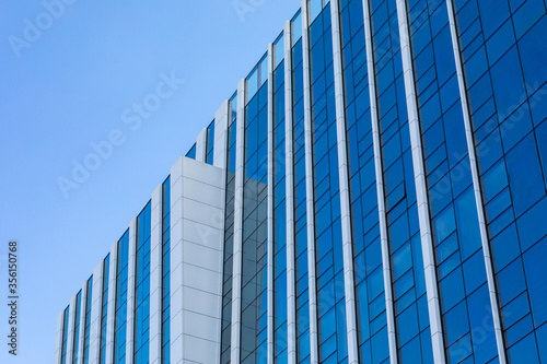 Part of a glass mirrored office building reflecting the blue sky. Exterior decoration of a hotel or shopping center with modern materials.