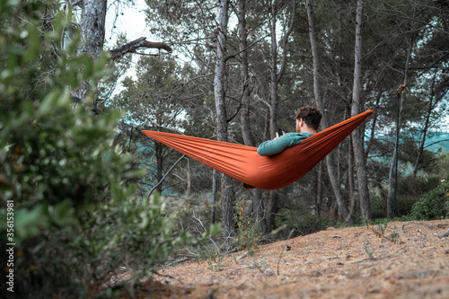 Man stretched out in a hammock while using his mobile