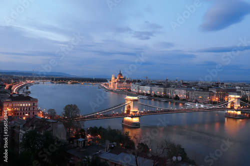 Budapest chain bridge and Parliament building illuminated at night by city lights with reflection in the danube river.