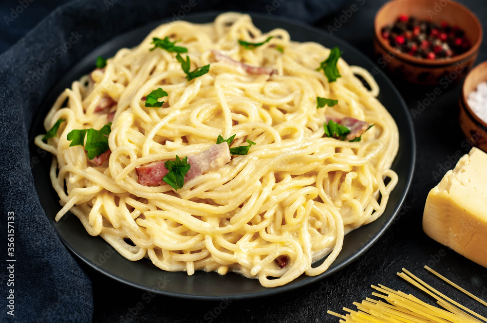 Homemade carbonara pasta in a black plate on a stone background