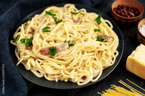 Homemade carbonara pasta in a black plate on a stone background
