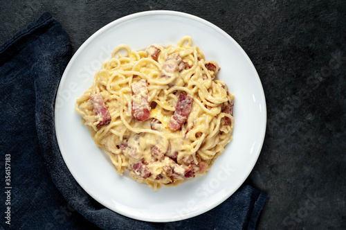 Homemade carbonara pasta in a white plate on a stone background
