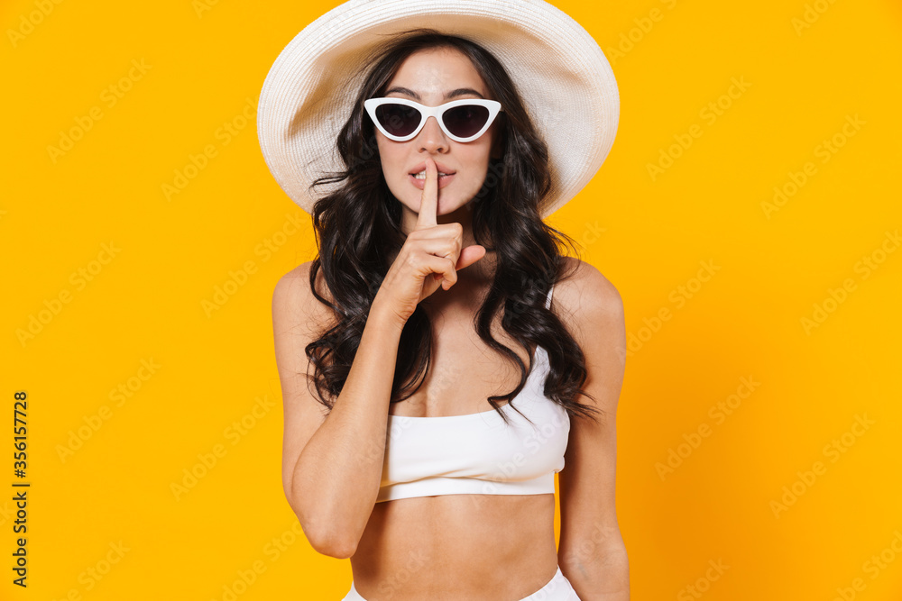 Image of pleased woman in swimsuit and hat making silence gesture