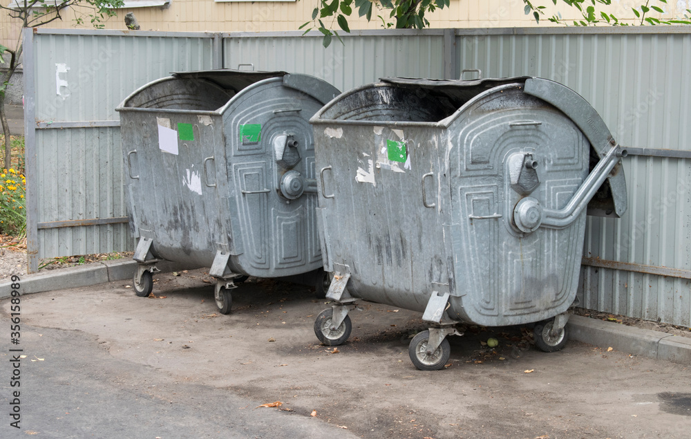 Two metal garbage containers on town street. Four wheeled trash cans Two metal garbage containers on town street. Four wheeled trash cans