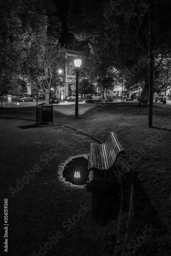 Piekny, nastrojowy widok nocnego parku z lawka, latarnia i jej odbiciem