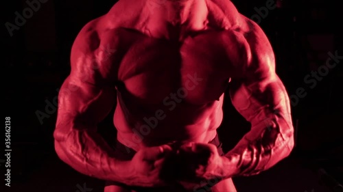 posing muscular bodybuilder in red light with a dark background