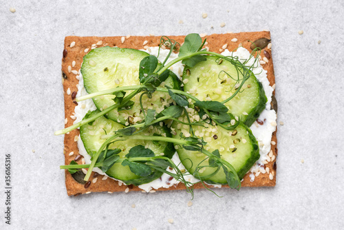 Rye crispbread with cream cheese, micro greens and cucumber garnished with hemp seeds. Healthy vegetarian snack. Grey concrete background photo