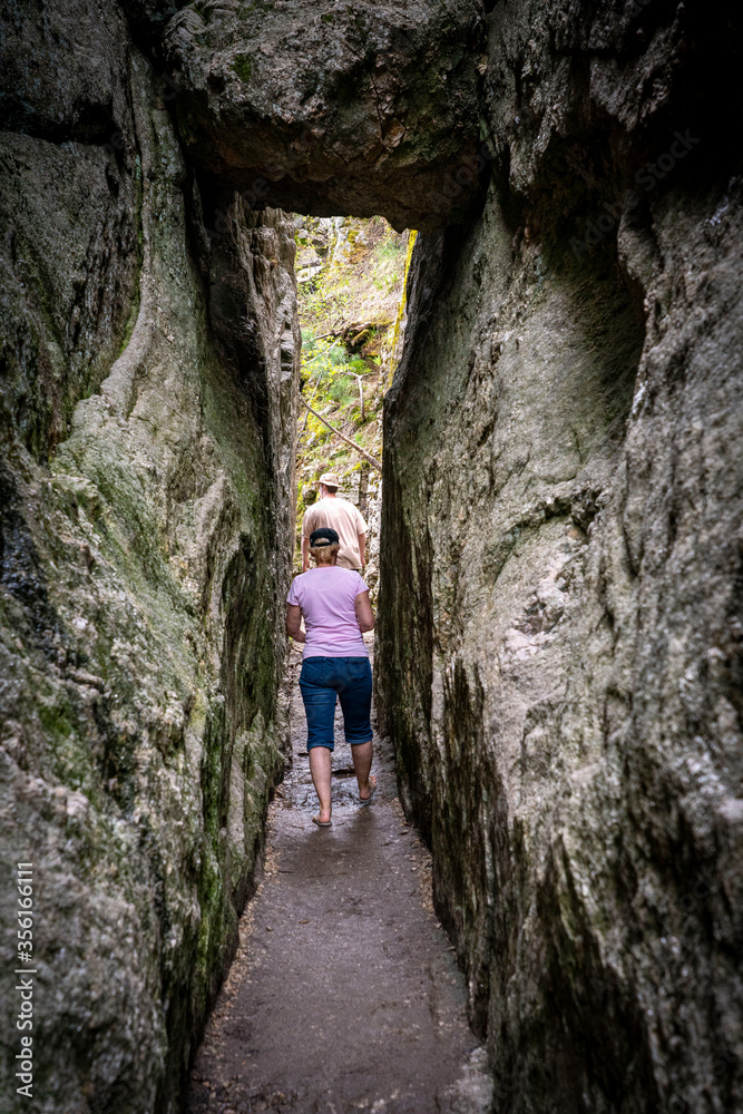 A young man and a woman hike through a narrow stone passageway in the rocky Black Hills of South Dakota, USA.