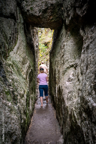 A young man and a woman hike through a narrow stone passageway in the rocky Black Hills of South Dakota, USA.