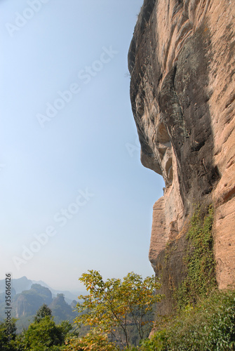 Wuyishan mountains in Fujian Province, China. On the path to DaWang (Great King) Peak. View over the mountains with a steep cliff and trees in the foreground. Wuyishan is a UNESCO site in China.