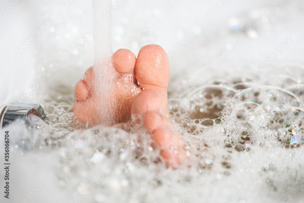 Baby feet in the bathroom with foam and bubbles close-up. Bathing in a bathtub with white foam Baby feet in the bathroom with foam and bubbles close-up. Bathing in a bathtub with white foam