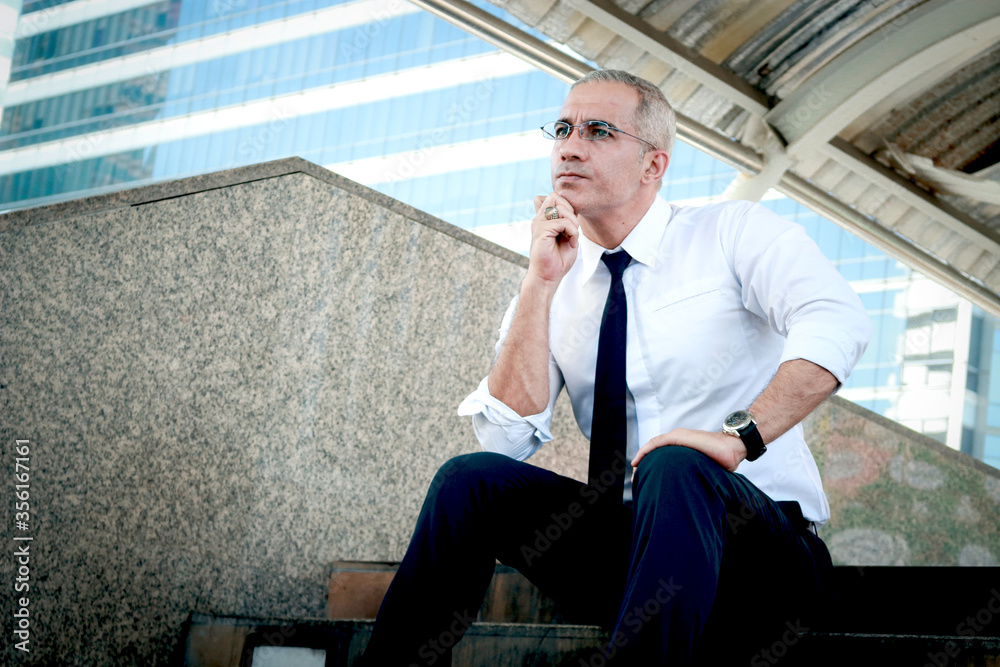 Senior businessman sitting on stairway outside office in downtown of modern city. Serious man resting chin on hand and thinking about his job. Senior businessman sitting on stairway outside office in downtown of modern city. Serious man resting chin on hand and thinking about his job.