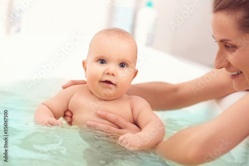 Fotografija Hands of a careful unknown mother hold a small beautiful funny big-eyed baby