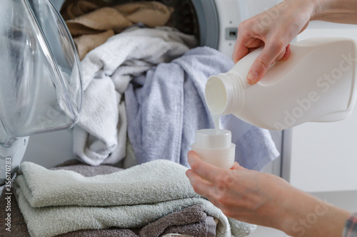 Obraz na płótnie Close up of female hands pouring liquid laundry detergent into cap. Washer machine and clothes with wicker basket in background w salonie