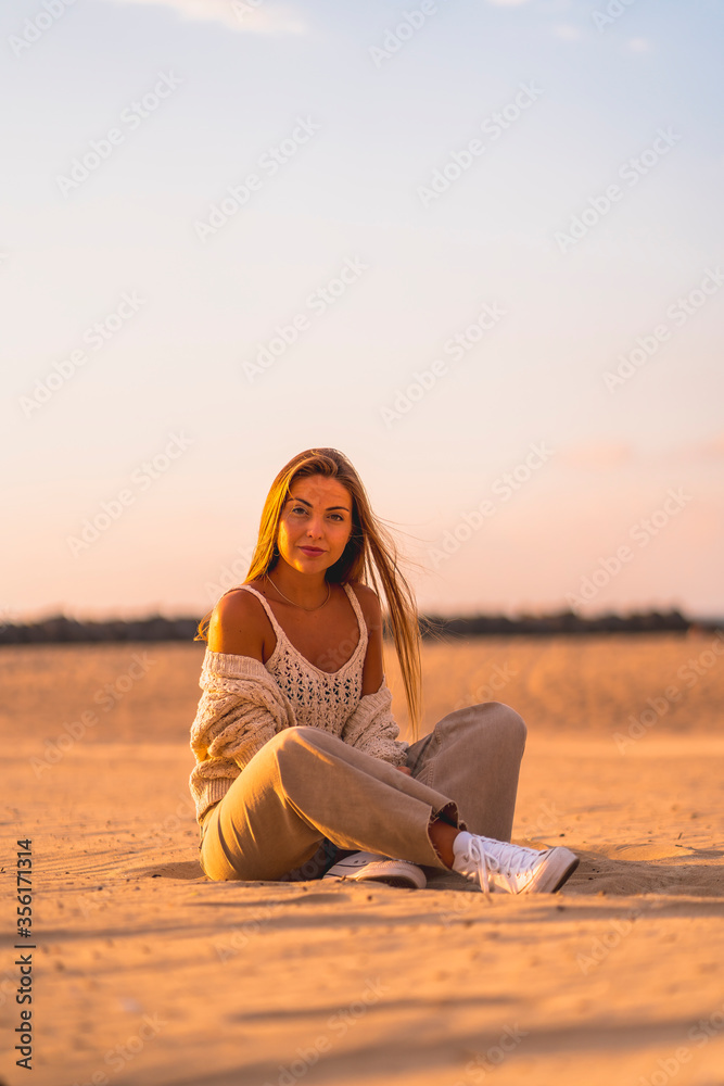 Summer lifestyle, a young blonde with straight hair, in a small wool sweater and corduroy pants sitting on the beach. Sitting in the serious sand