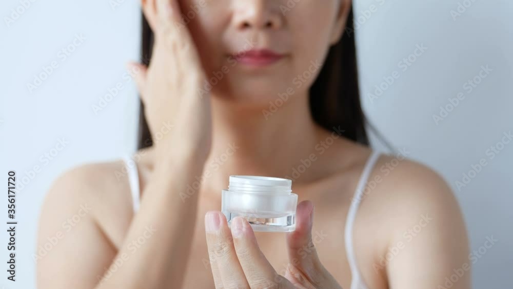 4K. cosmetic for beauty skincare, facial treatment concept. woman apply moisturizer lotion on her face from luxury white cosmetic cream packaging