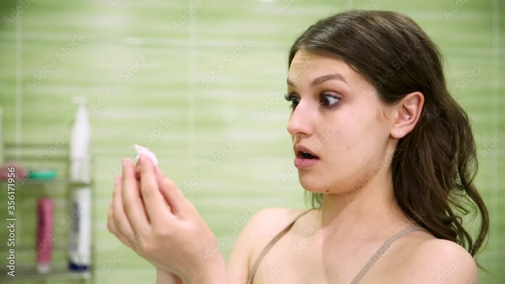 girl removes makeup using a cotton pad in a green bathroom girl removes makeup using a cotton pad in a green bathroom