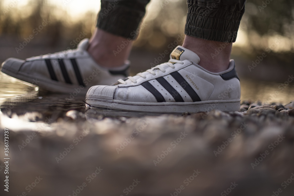 Young man wearing an old pair of Adidas Superstar shoes in a river water  Stock Photo | Adobe Stock