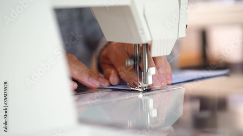 Slider shot of woman using hands to stitch a blue cotton face mask with a sewing machine. Homemade reusable medical protection 