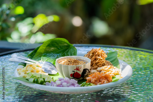 Miang kham – A royal leaf wrap appetizer, is a traditional Southeast Asian snack from Thailand and Laos. It's on the white dish in outdoor table with the sunlight. photo