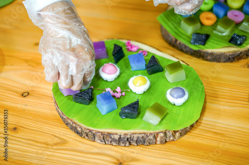 Thai Chef's hand is decorating Varieties traditional colorful Thai desserts set; steaming flour, black custard, coconut custard & steaming bean, layer pudding cake photo