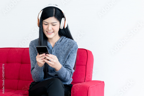 Portrait images of Asian attractive woman wearing headphones, using a mobile phone and Sitting on the red sofa On white background, concept to relaxation and entertainment