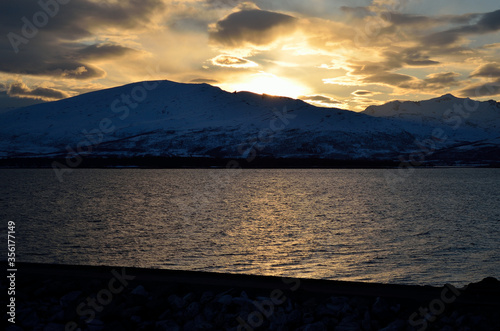 golden vibrant sunset over snowy mountain and fjord landscape