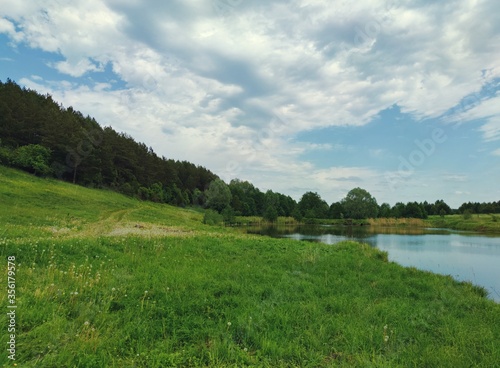 beautiful blue sky with clouds before the rain over a green meadow between the forest and the lake