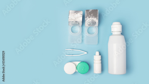 Contact lenses set with saline in bottle, tweezers, eye drops, plastic case with solution on blue background with copy space