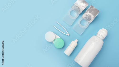 Contact lenses set with saline in bottle, tweezers, eye drops, plastic case with solution on blue background with copy space. Lifestyle