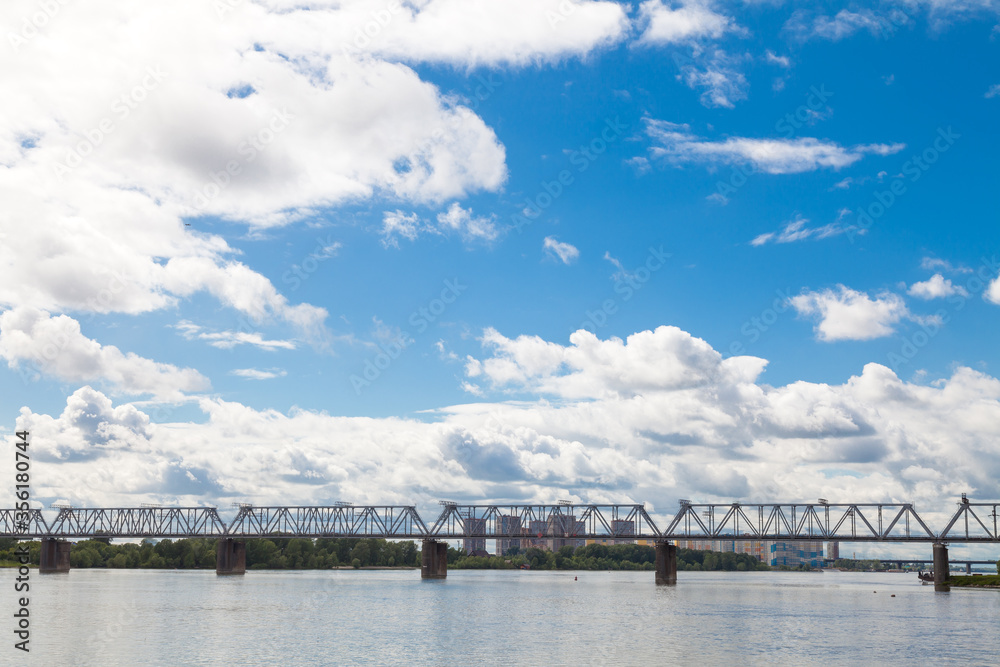 Railway bridge over the Ob river in Novosibirsk under a blue sky with white clouds. Picturesque landscapes of Russia.