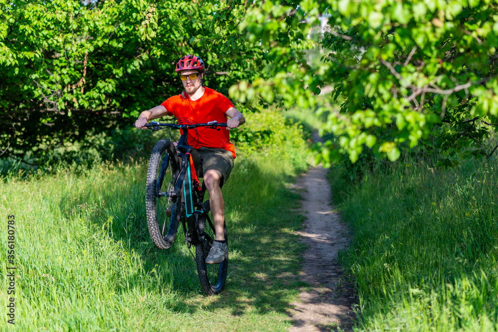 A cyclist rides on the rear wheel of a bicycle along a forest path. Active lifestyle, extreme.