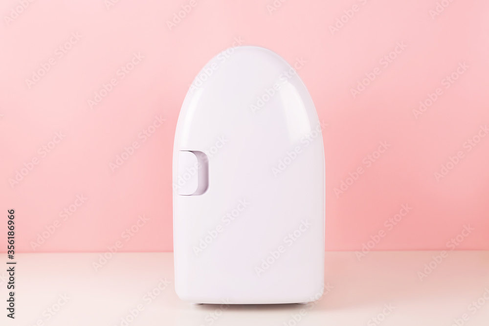 Mini fridge on pink background. Minimal composition. Trendy beauty item to keep skincare and makeup products cool and fresh.