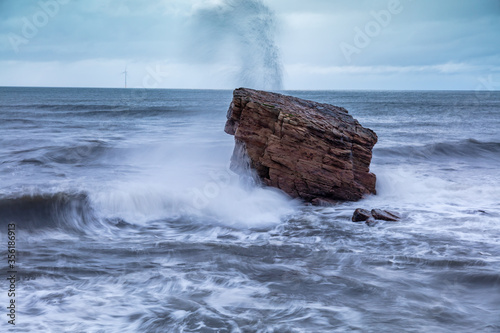 Rough Sea and brooding, stormy sky over Charlies Garden, rock pillar at Seaton Sluice on the coast of Northumberland, England, UK.