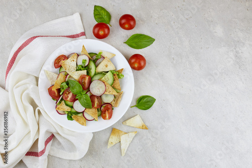 Fattoush or Arab (Lebanese) salad with pita bread, fresh vegetables and basil on plate on light background.