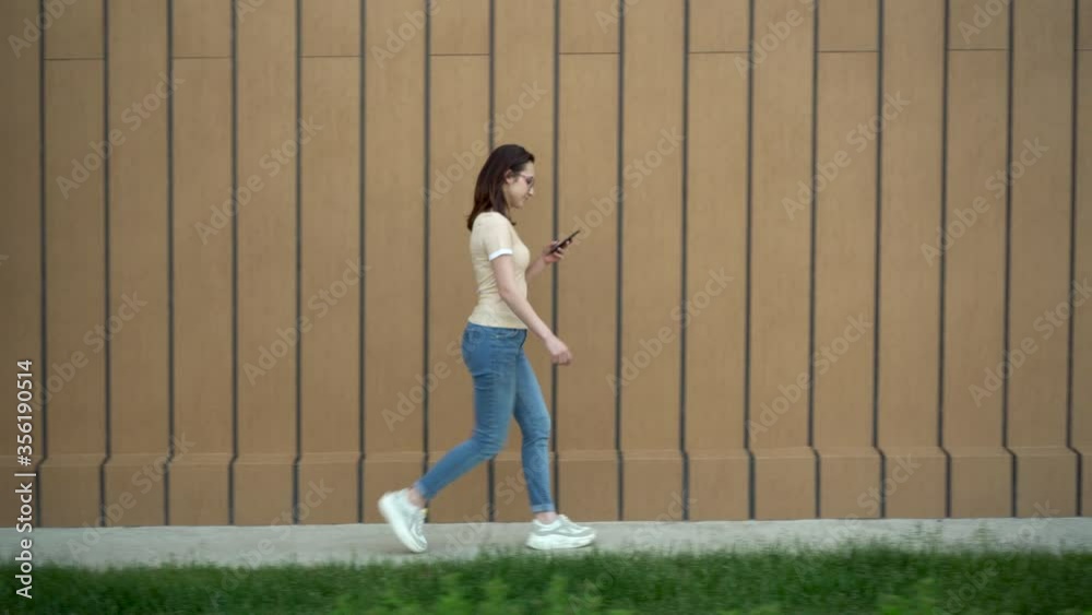 A young woman goes with a phone in her hand. A girl walks near the building and carries on correspondence in a smartphone.