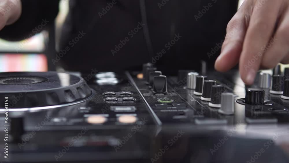 DJ sound control console for mixing dance music and laptop in disco club. Hands touching buttons sliders, playing electronic music on mixing deck, color illumination in nightclub dance party. Close up DJ sound control console for mixing dance music and laptop in disco club. Hands touching buttons sliders, playing electronic music on mixing deck, color illumination in nightclub dance party. Close up