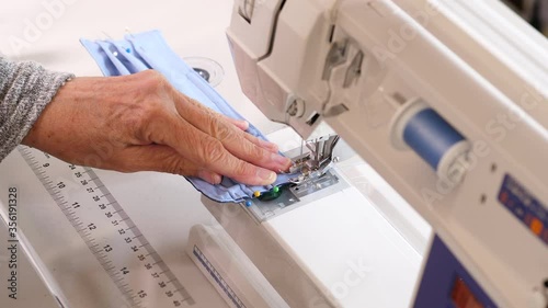 Stitching a homemade cotton face mask with a sewing machine. Female hands assemble a reusable cloth medical mask to prevent virus spread.