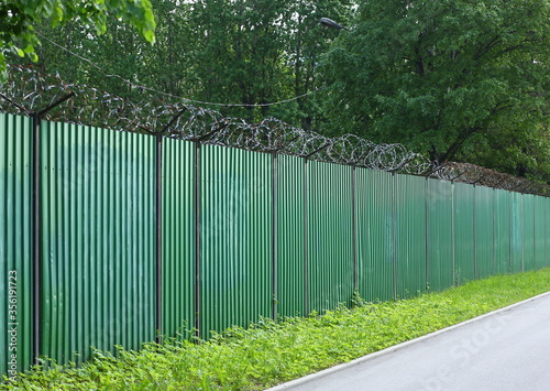 A green metal fence with barbed wire
