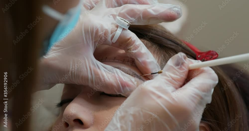 Cosmetologist applying permanent make up on woman eyebrow