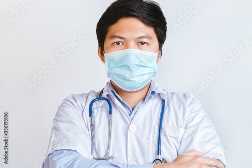 Portrait of handsome young doctor in white medical uniform and mask looking at camera against white background