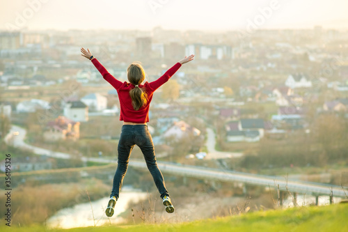 Young woman jumping with outstretched arms and legs outdoors on a distant city background. Relaxing, freedom and wellness concept.
