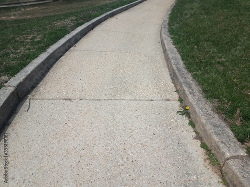 grey cement sidewalk or path with curb and green grass