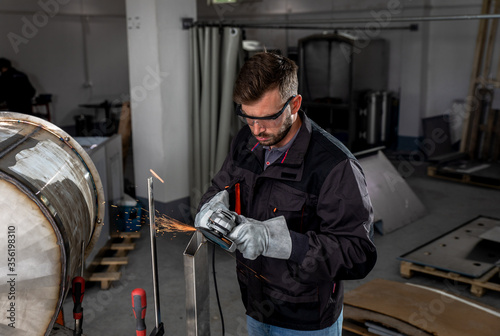 Industrial worker with angle grinder working and polishing metal structure at workshop.