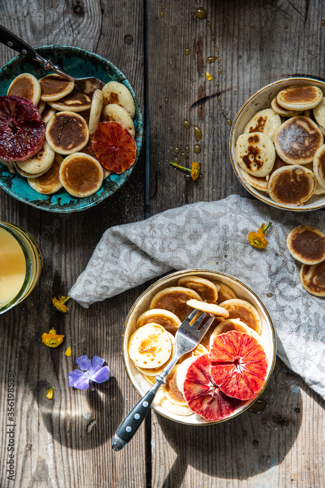 Ceramic bowl with mini pancakes, blood orange slices and honey on old wooden table. Ceramic bowl with mini pancakes, blood orange slices and honey on old wooden table.