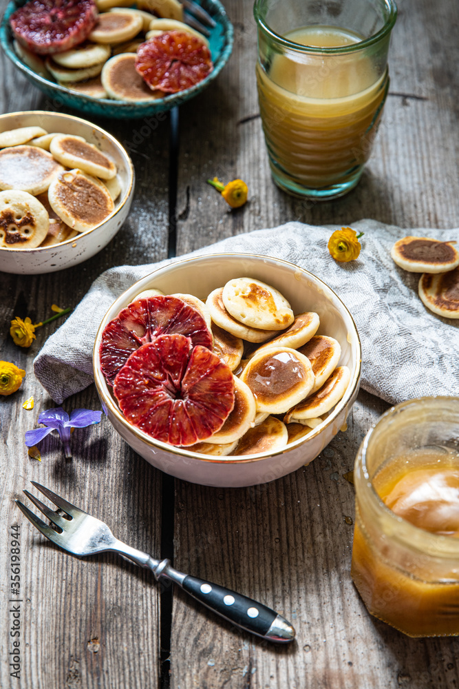 Ceramic bowl with mini pancakes, blood orange slices and honey on old wooden table. Ceramic bowl with mini pancakes, blood orange slices and honey on old wooden table.