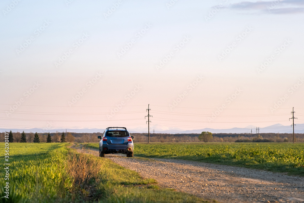 Landscape with blue off road car on gravel road. Traveling by auto, adventure in wildlife, expedition or extreme travel on a SUV automobile. Offroad 4x4 vehicle in field at sunrise.